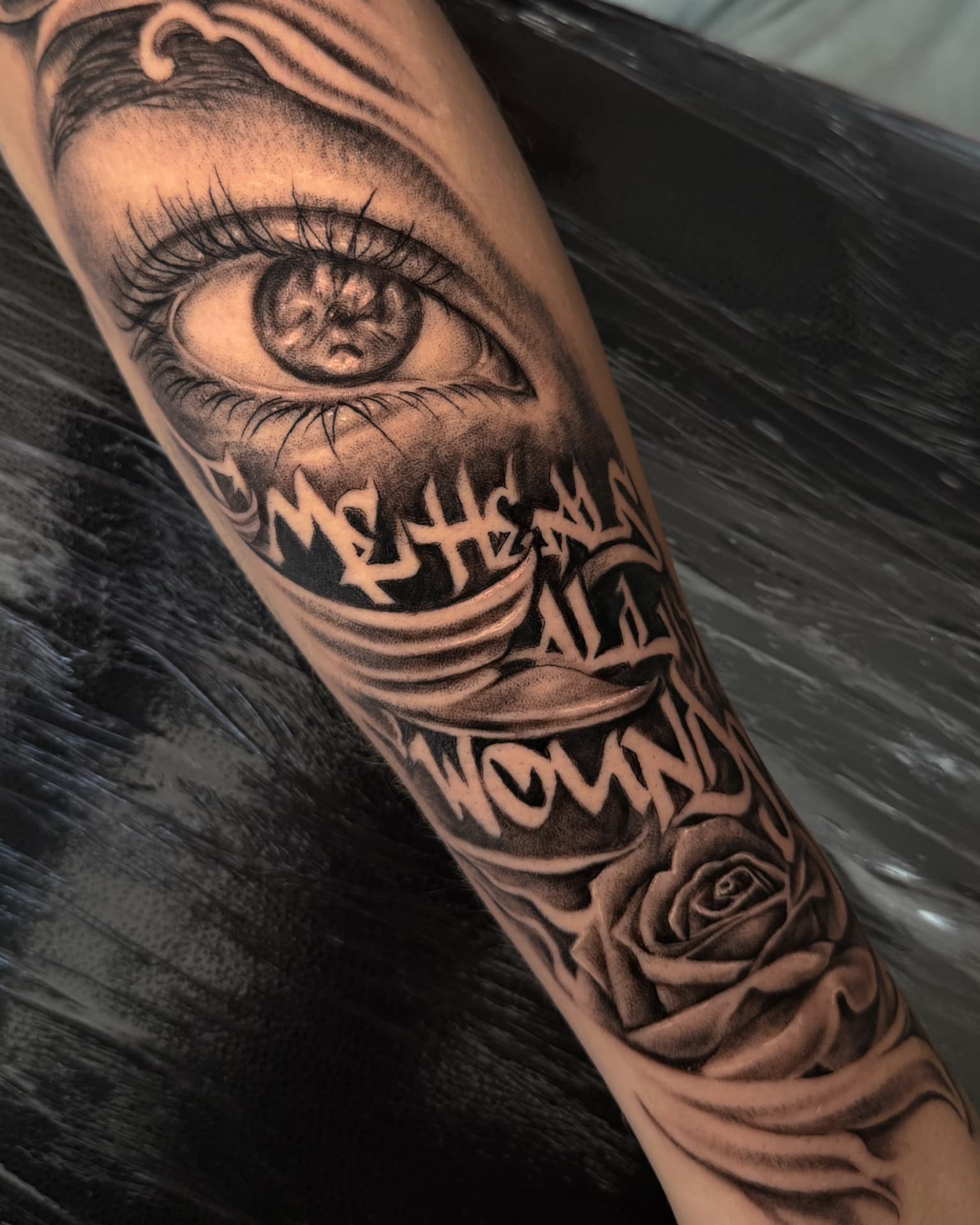 Forearm tattoo with a realistic eye, lettering and a rose by Wilson